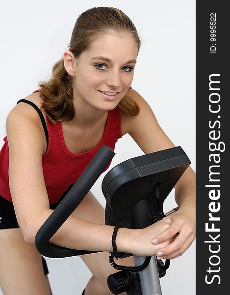 Young active woman in red sport shirt sitting on a bicycle ergometer. Young active woman in red sport shirt sitting on a bicycle ergometer