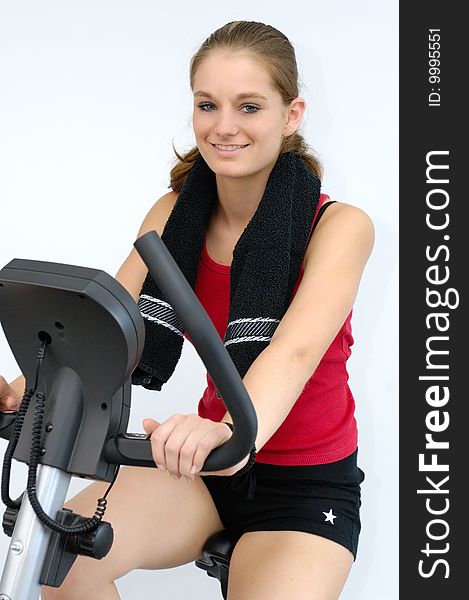 Young active woman in red sport shirt sitting on a bicycle ergometer. Young active woman in red sport shirt sitting on a bicycle ergometer