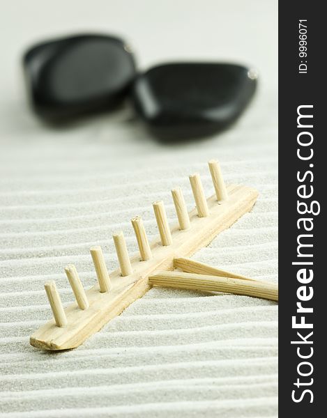 Black stones and wooden rake in the sand of an zen garden