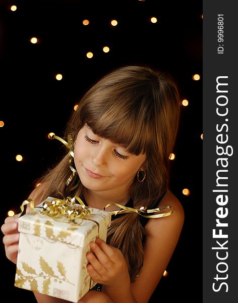 A cute young girl holding a christmas gift, dark background with christmas light bokeh