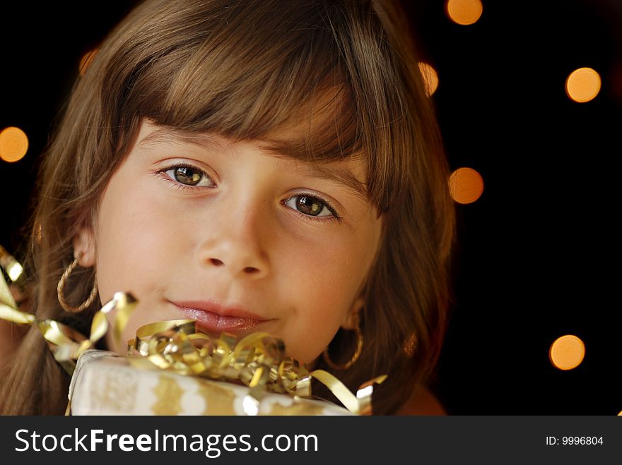 A beautiful young girl holding a gift, dark background with christmas light bokeh. A beautiful young girl holding a gift, dark background with christmas light bokeh