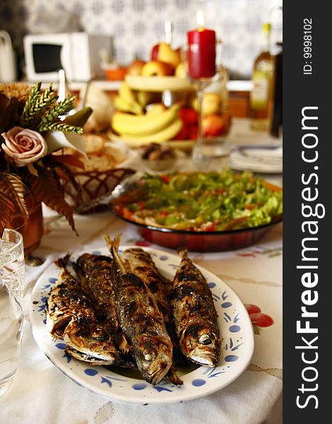 On the table, grilled mackerels poured with olive oil, water, salad, fruit and bread.