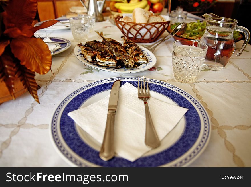 On the table, grilled mackerels poured with olive oil, water, salad, fruit and bread.
