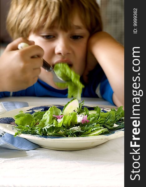 Young boy sits in front of a salad. Young boy sits in front of a salad