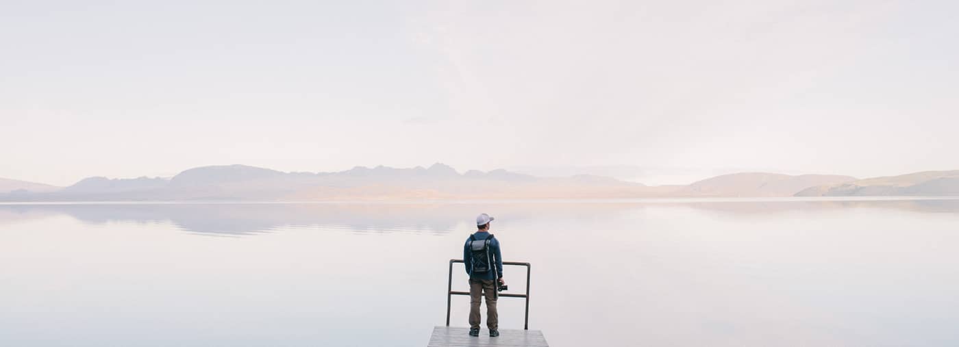 Man Wearing Jacket Standing on Wooden Docks Leading to Body of Water