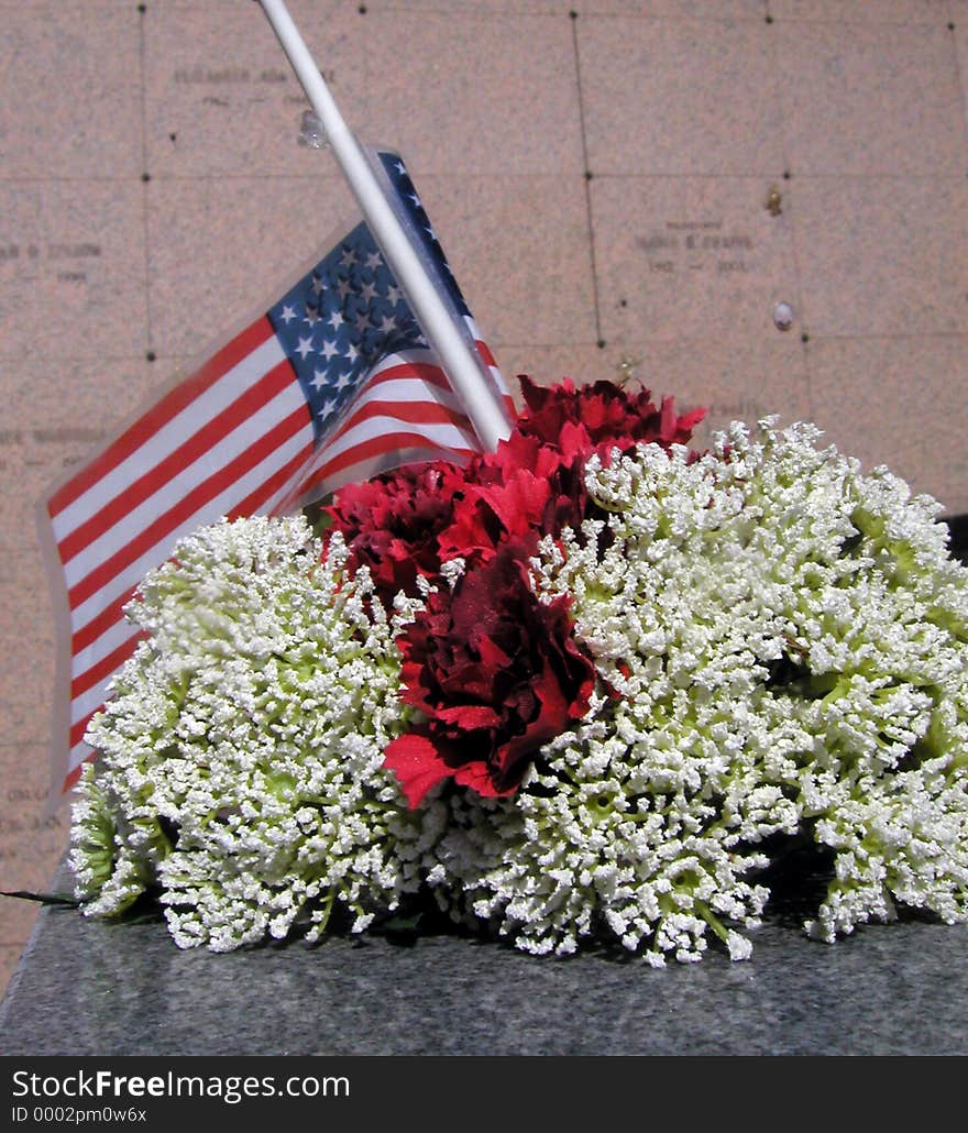 Flowers and a plastic flag left in memory of a loved one at a cemetery. The names engraved in the background have been blurred so they aren't readable. Flowers and a plastic flag left in memory of a loved one at a cemetery. The names engraved in the background have been blurred so they aren't readable.