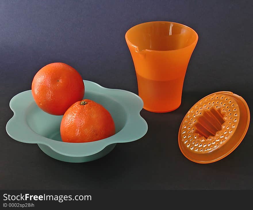 A set with squeezer, two fresh oranges on a blue plastic dish, on a black background. A set with squeezer, two fresh oranges on a blue plastic dish, on a black background