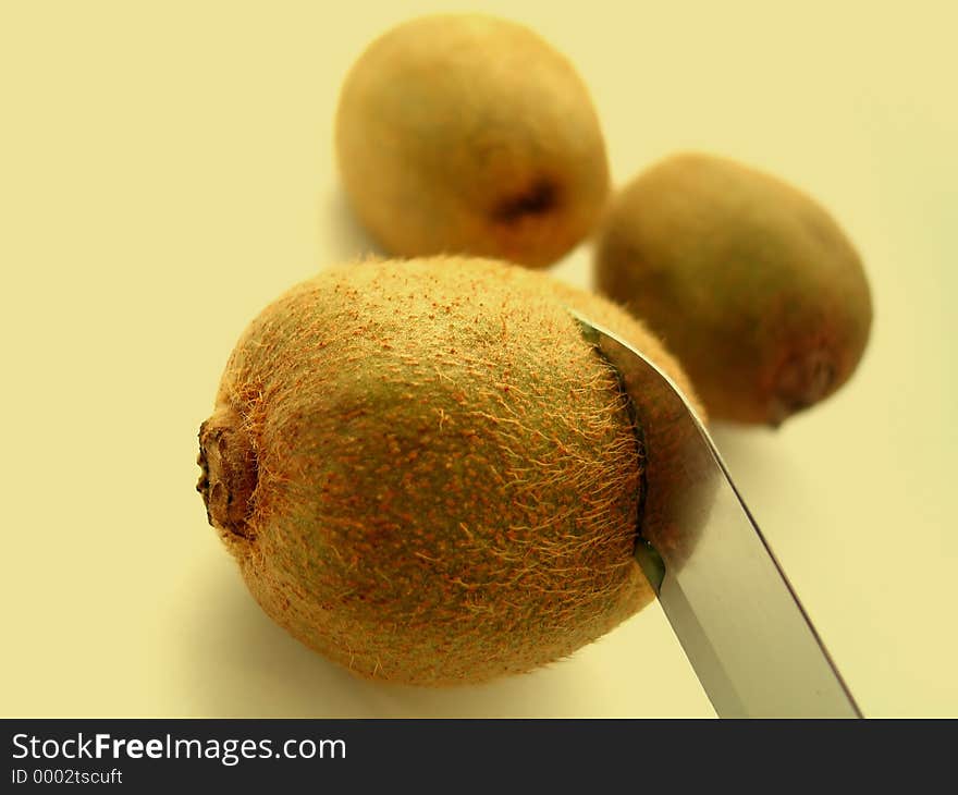 Three kiwi, focus on kiwi with knife cutting through it.