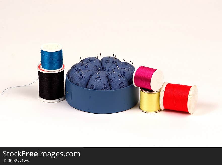 Pin cushion with pins sticking in it and surrounded by different colors of spools of thread. Pin cushion with pins sticking in it and surrounded by different colors of spools of thread