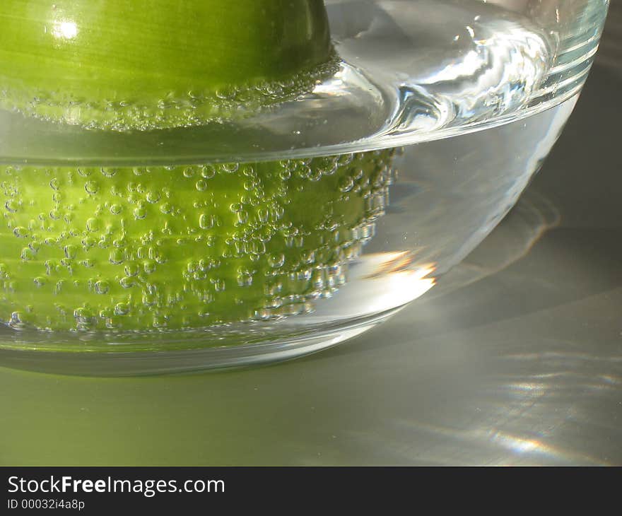 A green apple in a glass of sparkling mineral water. A green apple in a glass of sparkling mineral water.