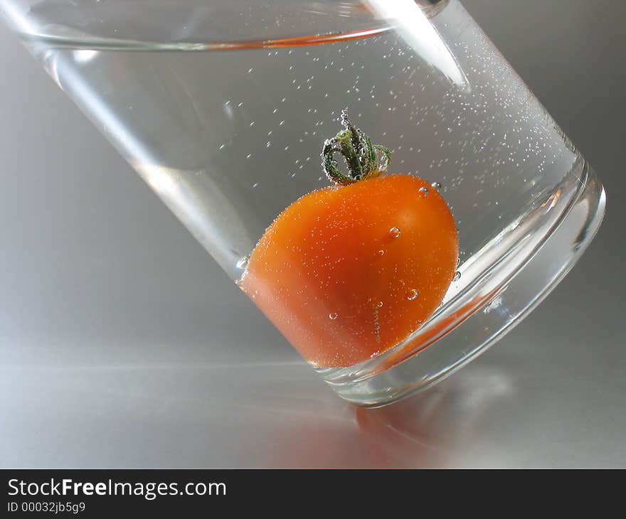 A red tomato in a glass filled with sparkling mineral water. A red tomato in a glass filled with sparkling mineral water.