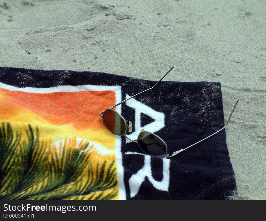 A beach towel, with sunglasses on it, sitting in the sand. A beach towel, with sunglasses on it, sitting in the sand