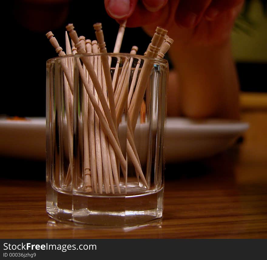 After the lunch this is an usual attitude: the hand pick up a toothpick from a glass.In the blurred background,you can see the plate in which was the food. After the lunch this is an usual attitude: the hand pick up a toothpick from a glass.In the blurred background,you can see the plate in which was the food.