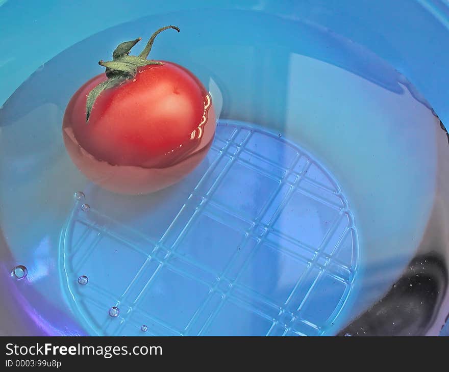 A tomato floating in water in a blue translucent bowl. A tomato floating in water in a blue translucent bowl