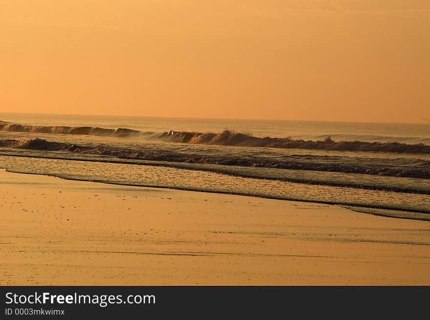 Waves breaking on the beach are turned a light shade of orange from the rising sun. Emerald Isle, North Carolina. Waves breaking on the beach are turned a light shade of orange from the rising sun. Emerald Isle, North Carolina