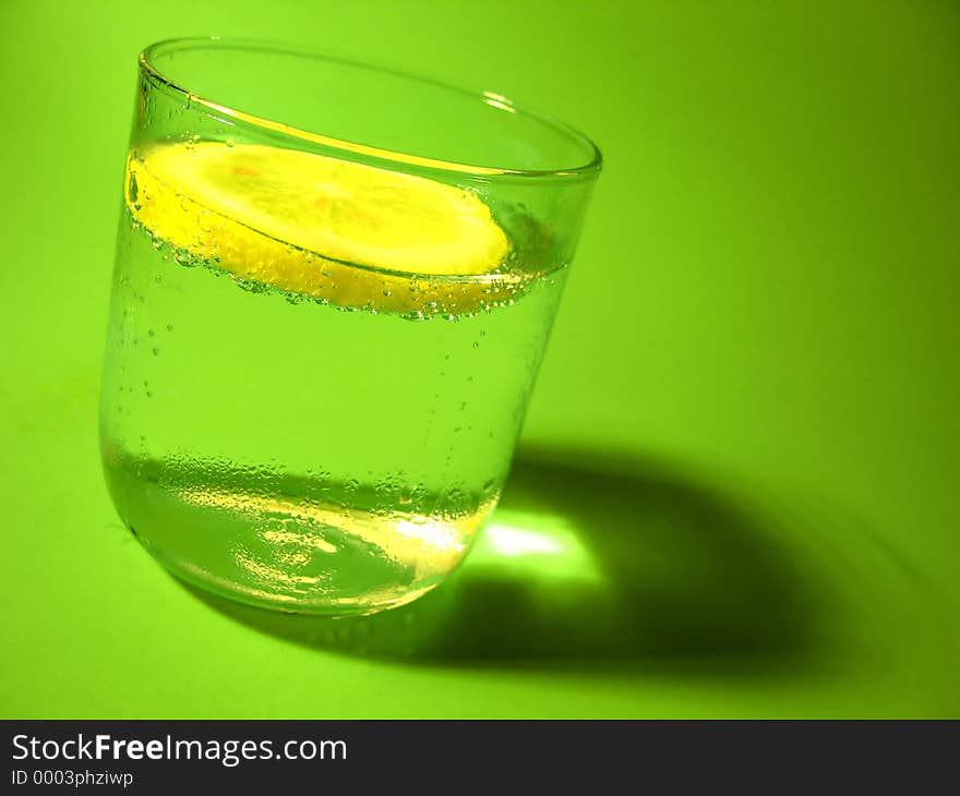 A glass of carbonated water with a lemon slice and vibrant green background. A glass of carbonated water with a lemon slice and vibrant green background.