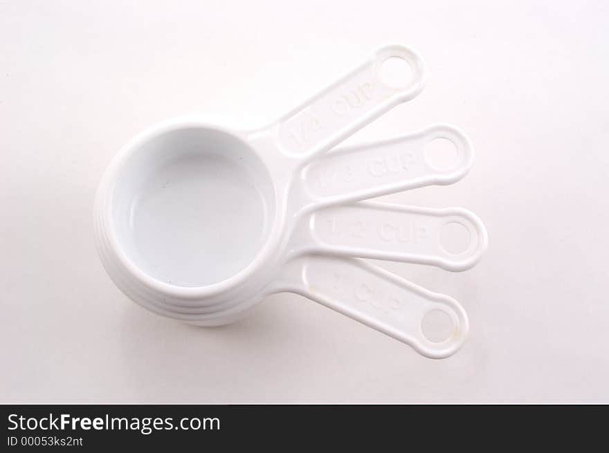 White measuring cups stacked on a white background with their handles fanned. White measuring cups stacked on a white background with their handles fanned.