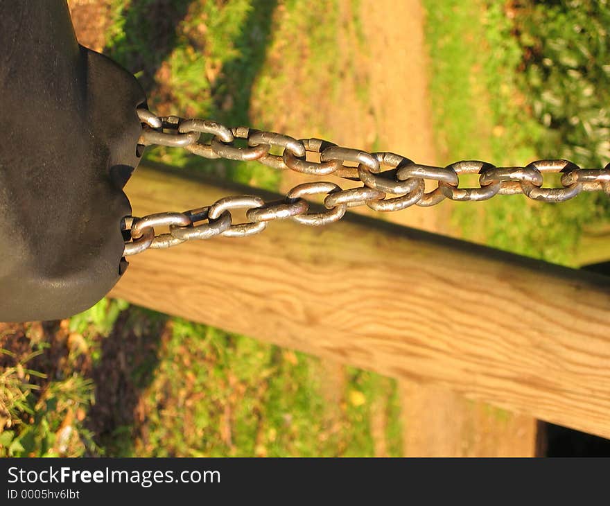 A rubber swing seat hanging on chains on a wooden frame. A rubber swing seat hanging on chains on a wooden frame.