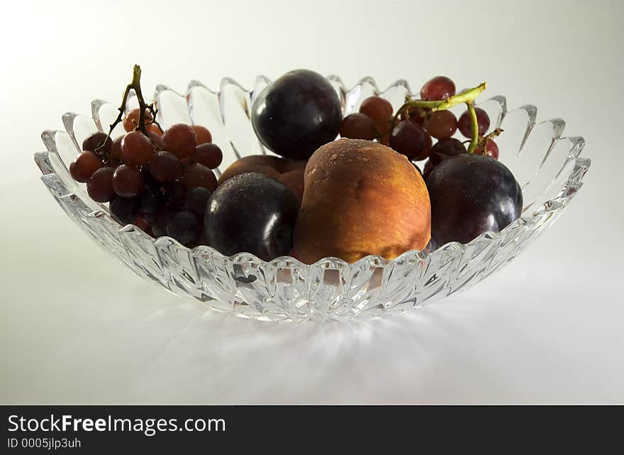 A crystal bowl filled with fruit, including peaches plums and grapes. A crystal bowl filled with fruit, including peaches plums and grapes