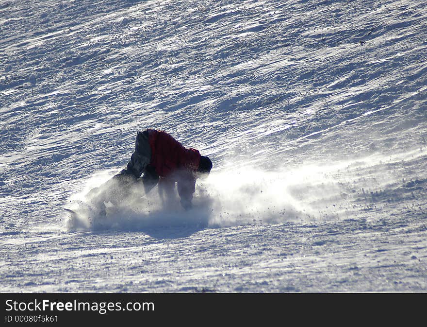 A snowboarder descending down a snow slope and wiping out at the bottom. A snowboarder descending down a snow slope and wiping out at the bottom.