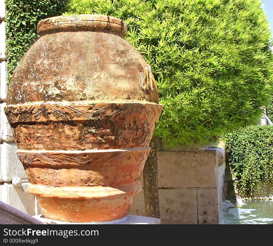 Red clay pot next to globularly-shaped tree, in garden of museum. Red clay pot next to globularly-shaped tree, in garden of museum