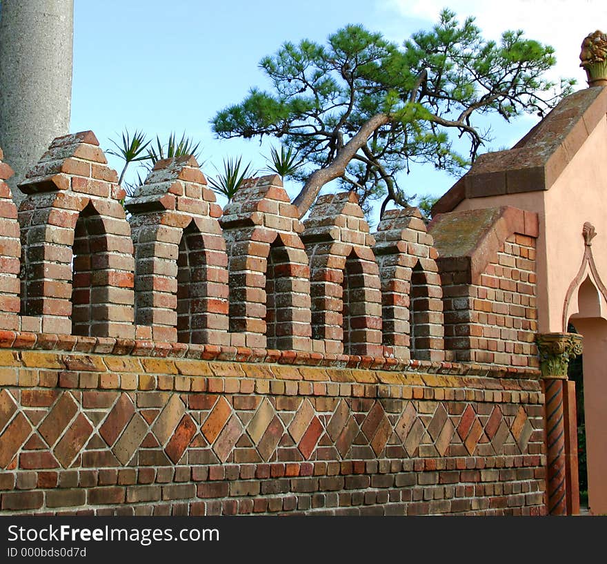 Multi-colored brick wall with decorative arches on top, with background of pine tree and blue sky. Multi-colored brick wall with decorative arches on top, with background of pine tree and blue sky