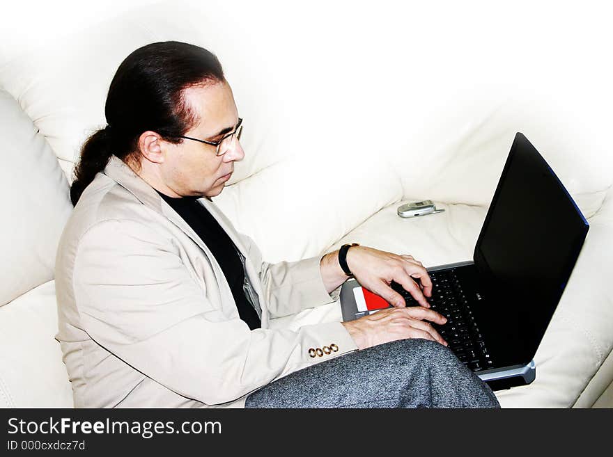 The man works behind a computer on a sofa. The man works behind a computer on a sofa