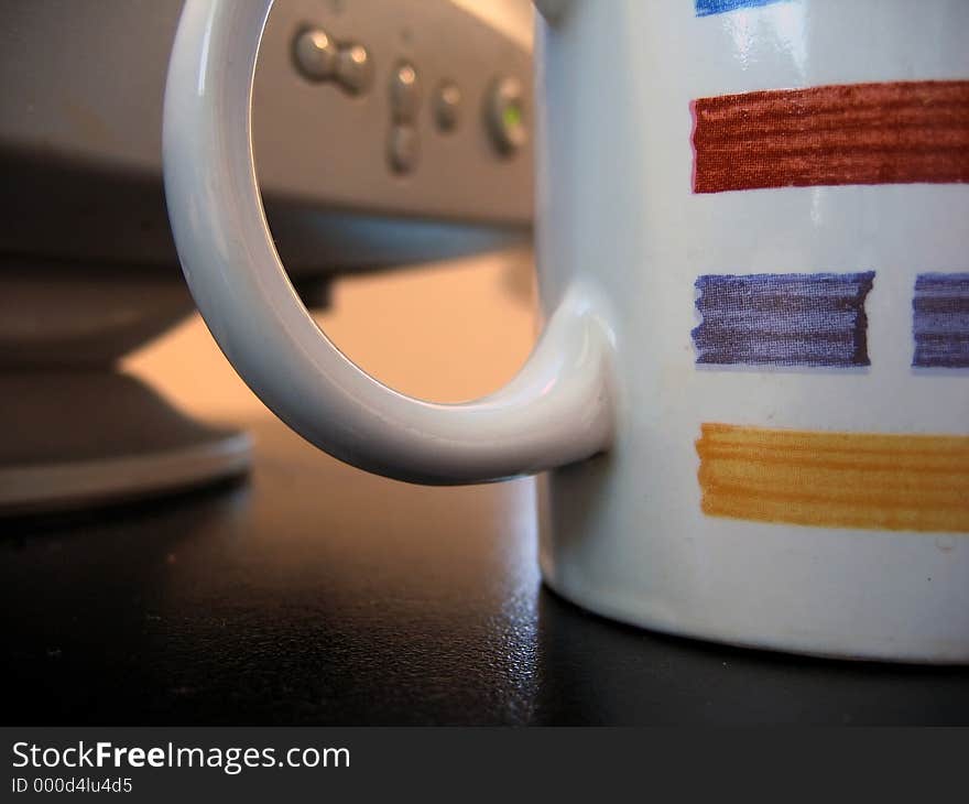 Monitor controls seen through handle of coffee mug, focus on mug. Monitor controls seen through handle of coffee mug, focus on mug