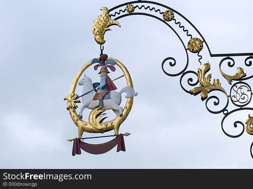 A decorative bar sign overhangs a sidewalk inFrance.