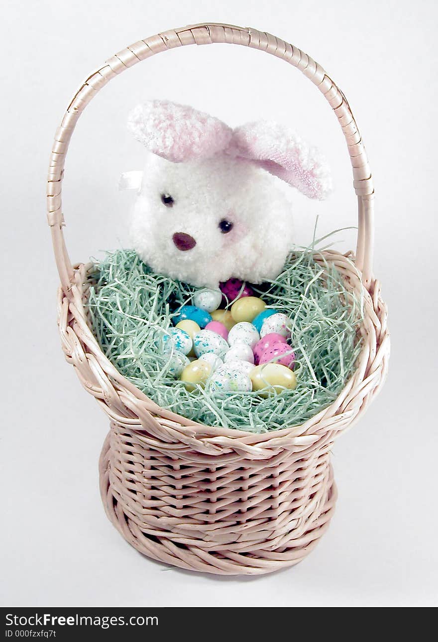 A cute stuffed bunny peeking into an Easter basket filled with fake grass and candy eggs. A cute stuffed bunny peeking into an Easter basket filled with fake grass and candy eggs.