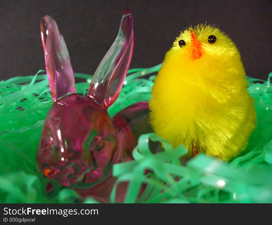 A rose glass bunny with a young chick in a nest of grass. A rose glass bunny with a young chick in a nest of grass.