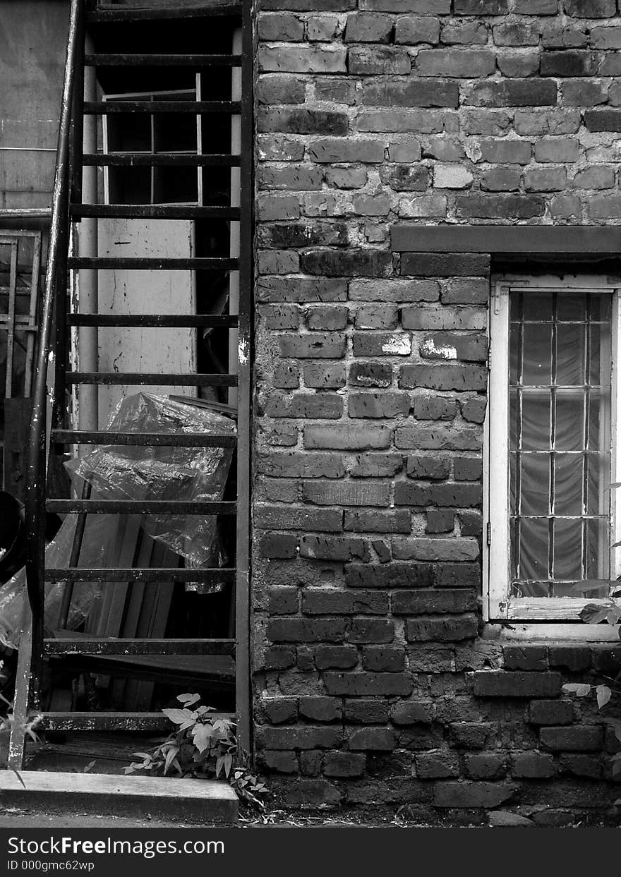 Black and white view of an old iron staircase and window in a brick wall. Black and white view of an old iron staircase and window in a brick wall.