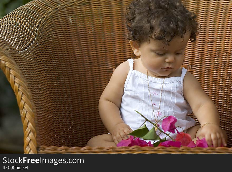 Infant sitting on a big wicker chair playing with an orchid. Infant sitting on a big wicker chair playing with an orchid