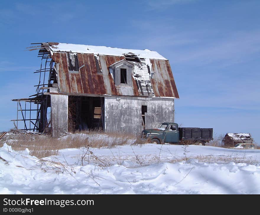 A decrepit barn and farm truck stand vigil in a wintry field. A decrepit barn and farm truck stand vigil in a wintry field.