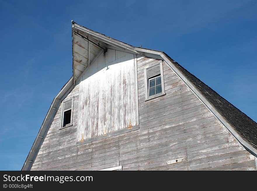 Top of a barn with worn white paint and broken windows. Top of a barn with worn white paint and broken windows