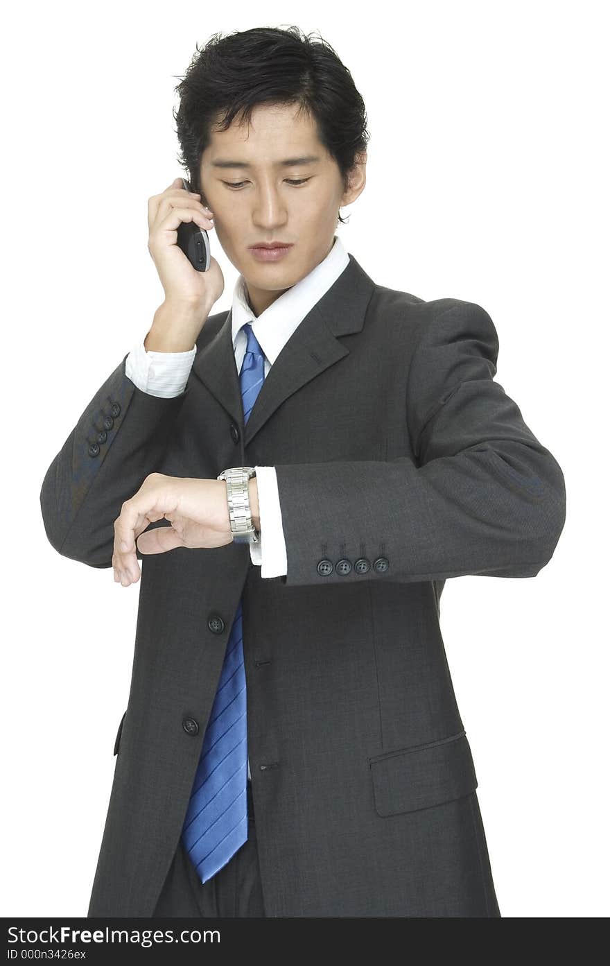 An asian businessman checks the time whist taking on the telephone. An asian businessman checks the time whist taking on the telephone