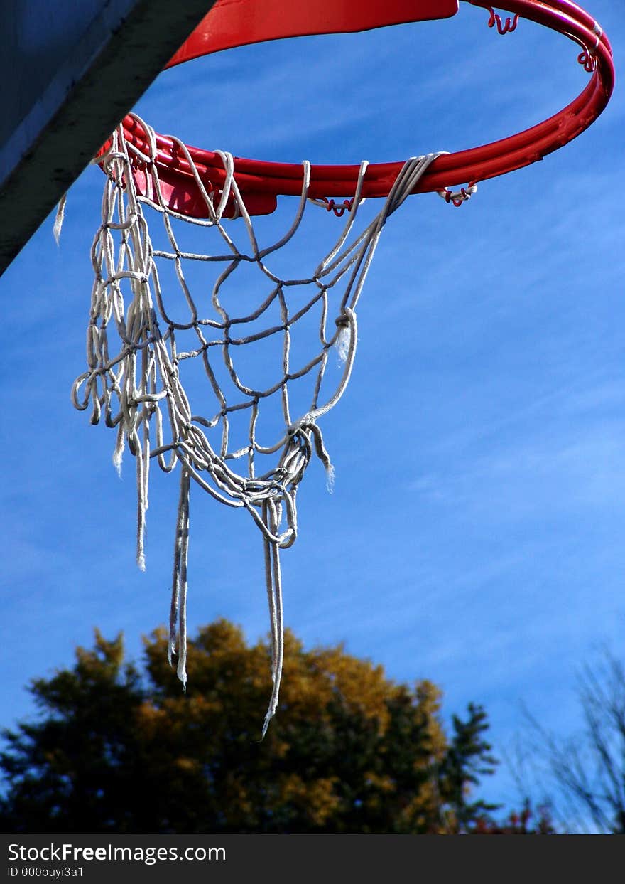 Orange basketball hoop with white tattered strings set off against a rich blue sky, trees in the background, easthampton, massachusetts. Orange basketball hoop with white tattered strings set off against a rich blue sky, trees in the background, easthampton, massachusetts