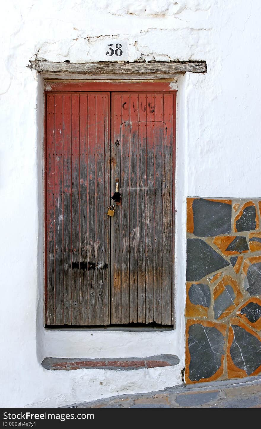 Old wooden padlocked door with peeling red paint on an old Spanish street.