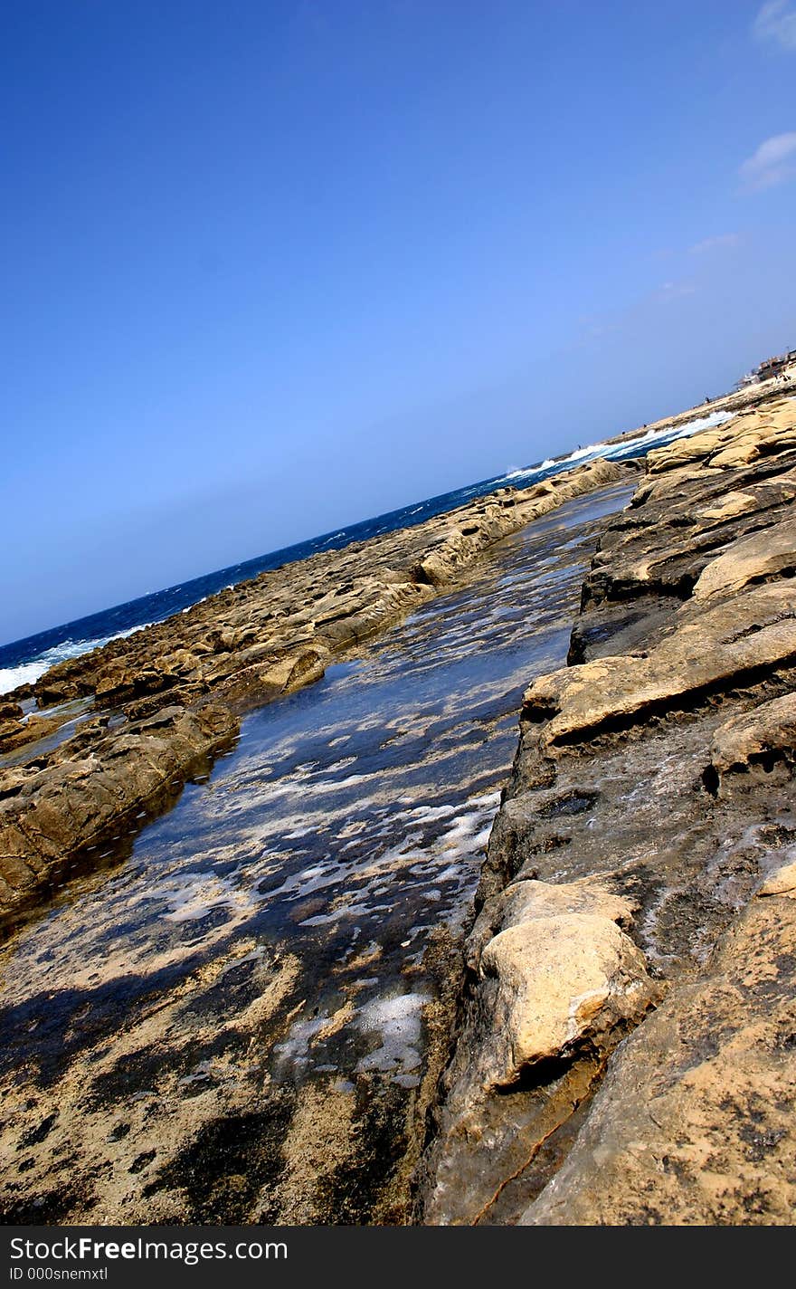 A wave cut canal on the shores of a limestone rocky beach in Malta.