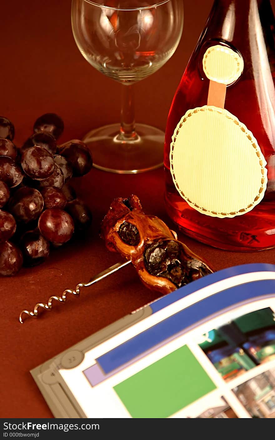 Bottle of Rose wine with blank label, an empty glass, red grapes, a corkscrew with wooden handle and blank magazine.