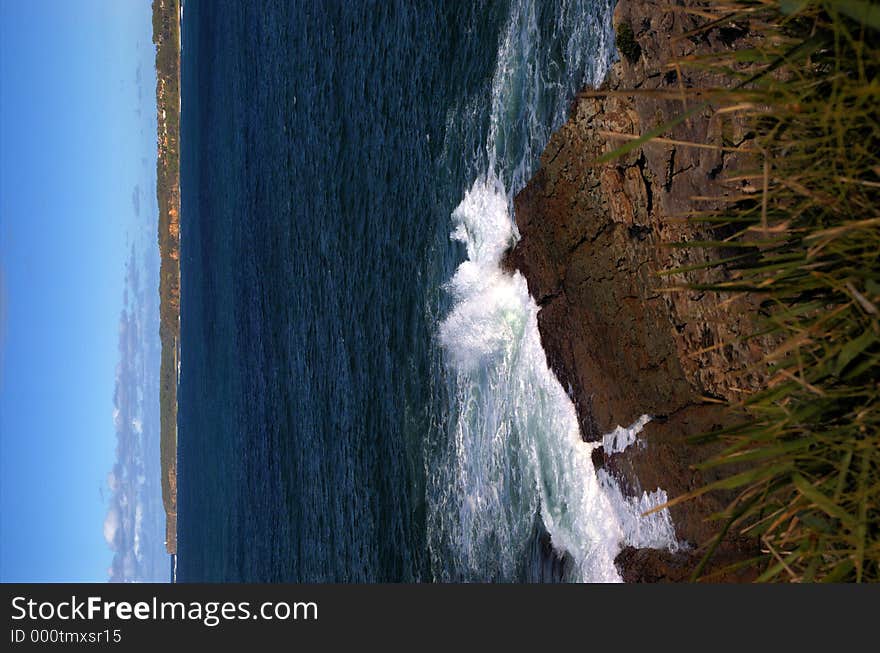 Waves crash against a rock shelf with a cliffline in the distance. Waves crash against a rock shelf with a cliffline in the distance