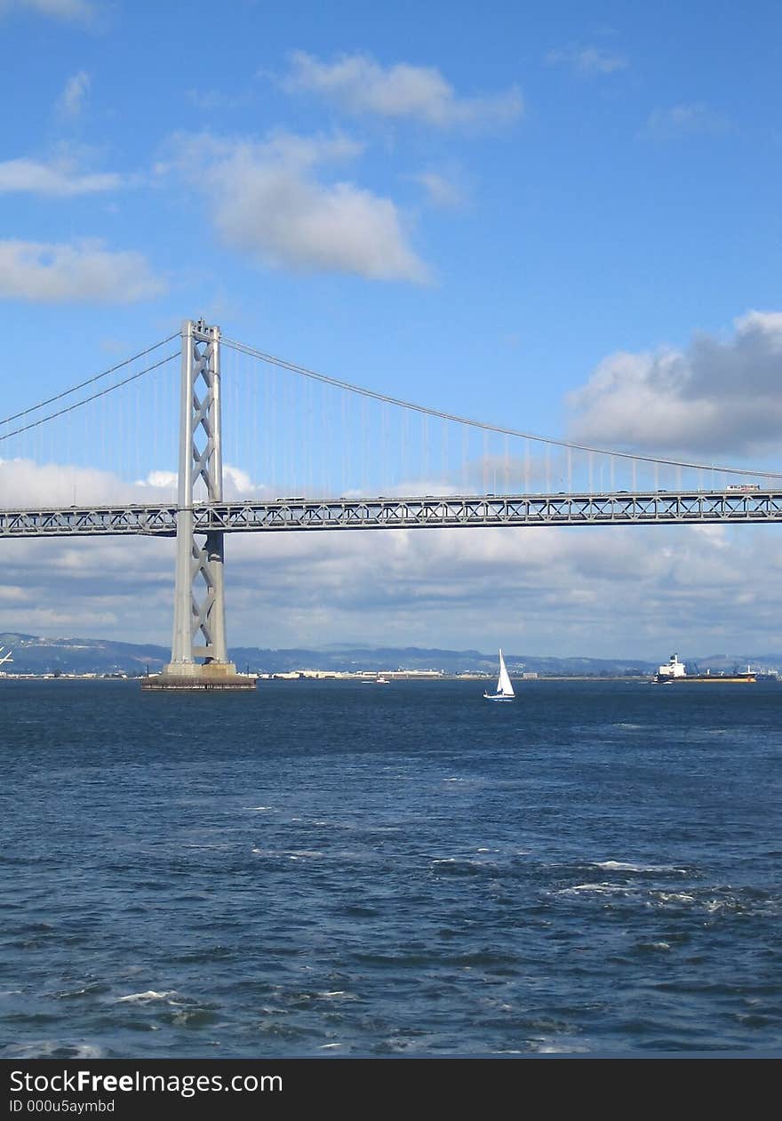 Bright day view of the San Francisco Bay Bridge, with cloud formations. Tall photo with Plenty of sea/water and sky space for titles. Bright day view of the San Francisco Bay Bridge, with cloud formations. Tall photo with Plenty of sea/water and sky space for titles.