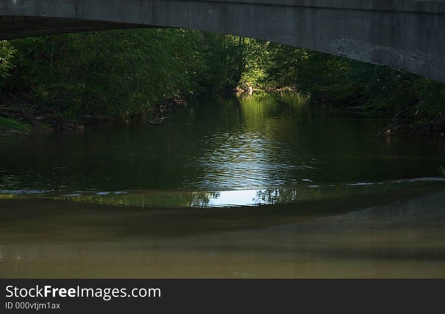 A view of a river showing a well lit part of the stream in the distance while the rest of the scene falls in shadow. A view of a river showing a well lit part of the stream in the distance while the rest of the scene falls in shadow