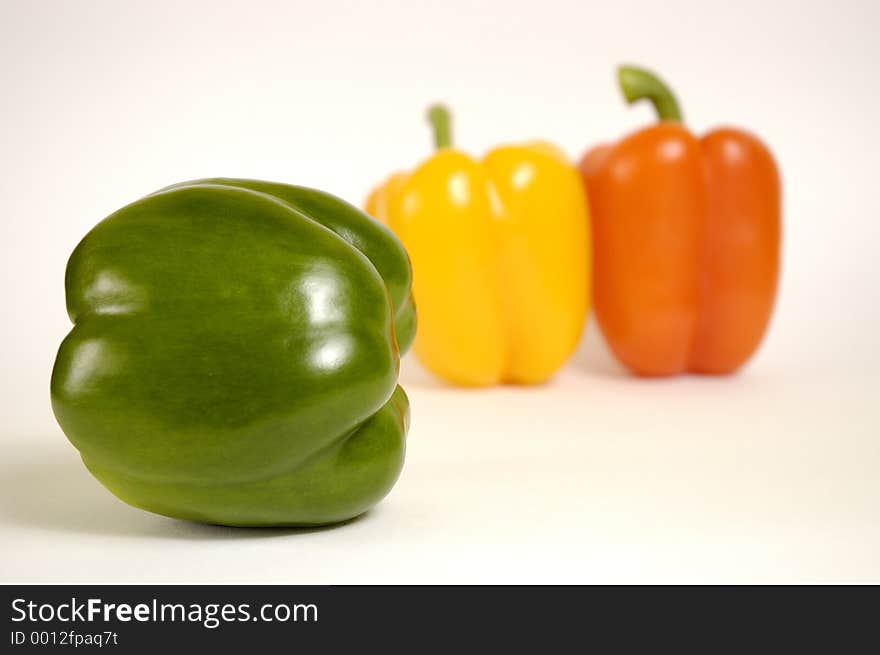 Green, yellow and orange paprika on a white background.