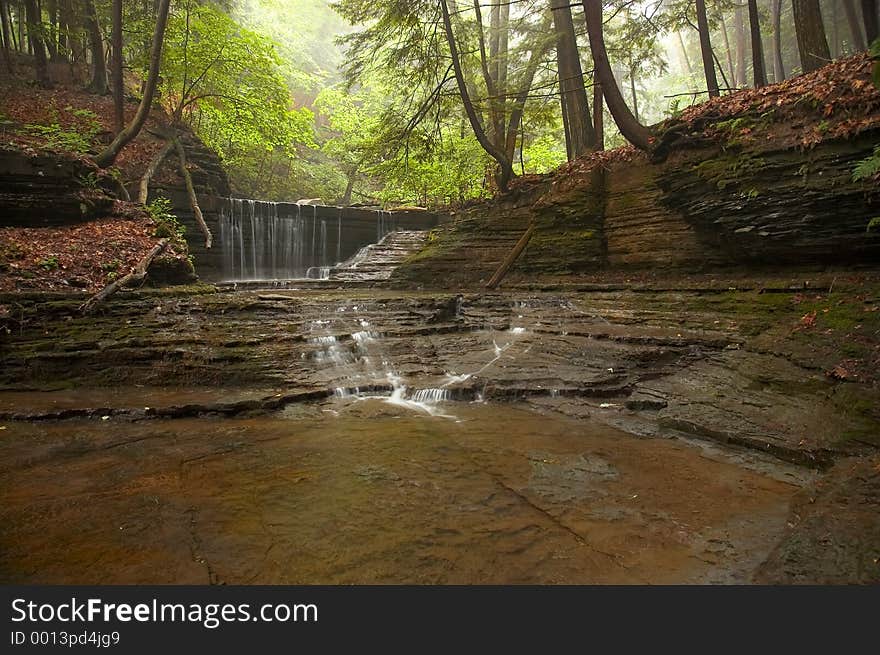 Small waterfall in the early morning light with some mist and fog in the background..