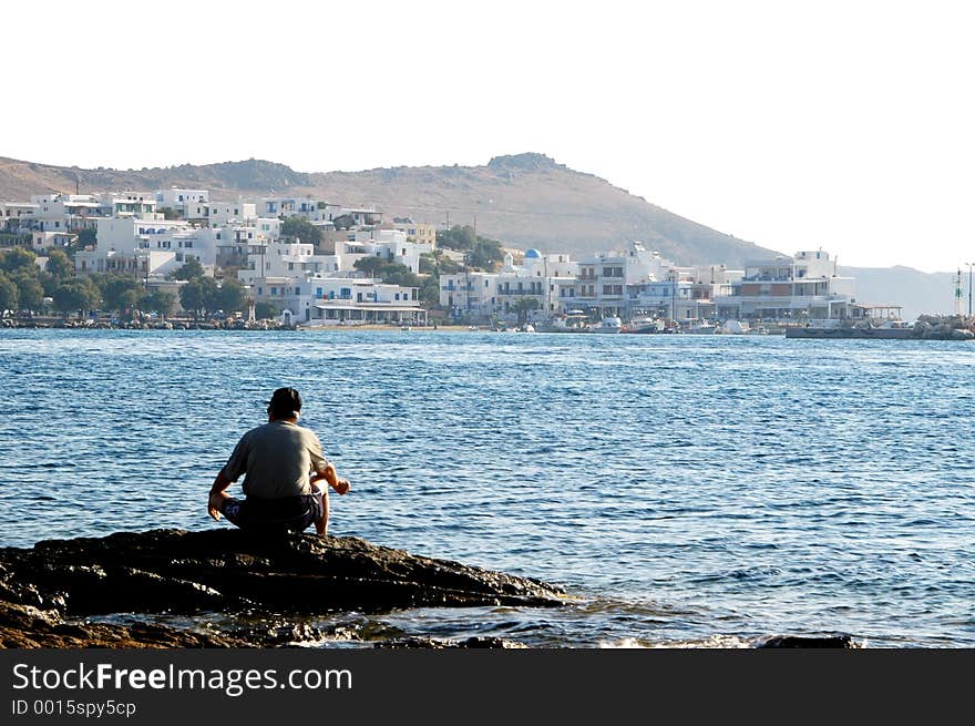 A man fishing in the greek islands with typical architecture in the distance