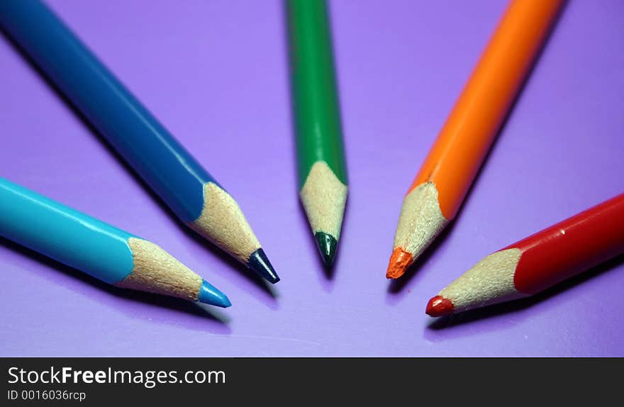 Blue, light blue, orange and red color pencils on a purple background. Blue, light blue, orange and red color pencils on a purple background