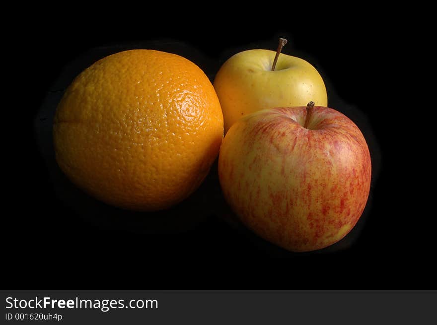 Two apples and an orange together over black. Two apples and an orange together over black