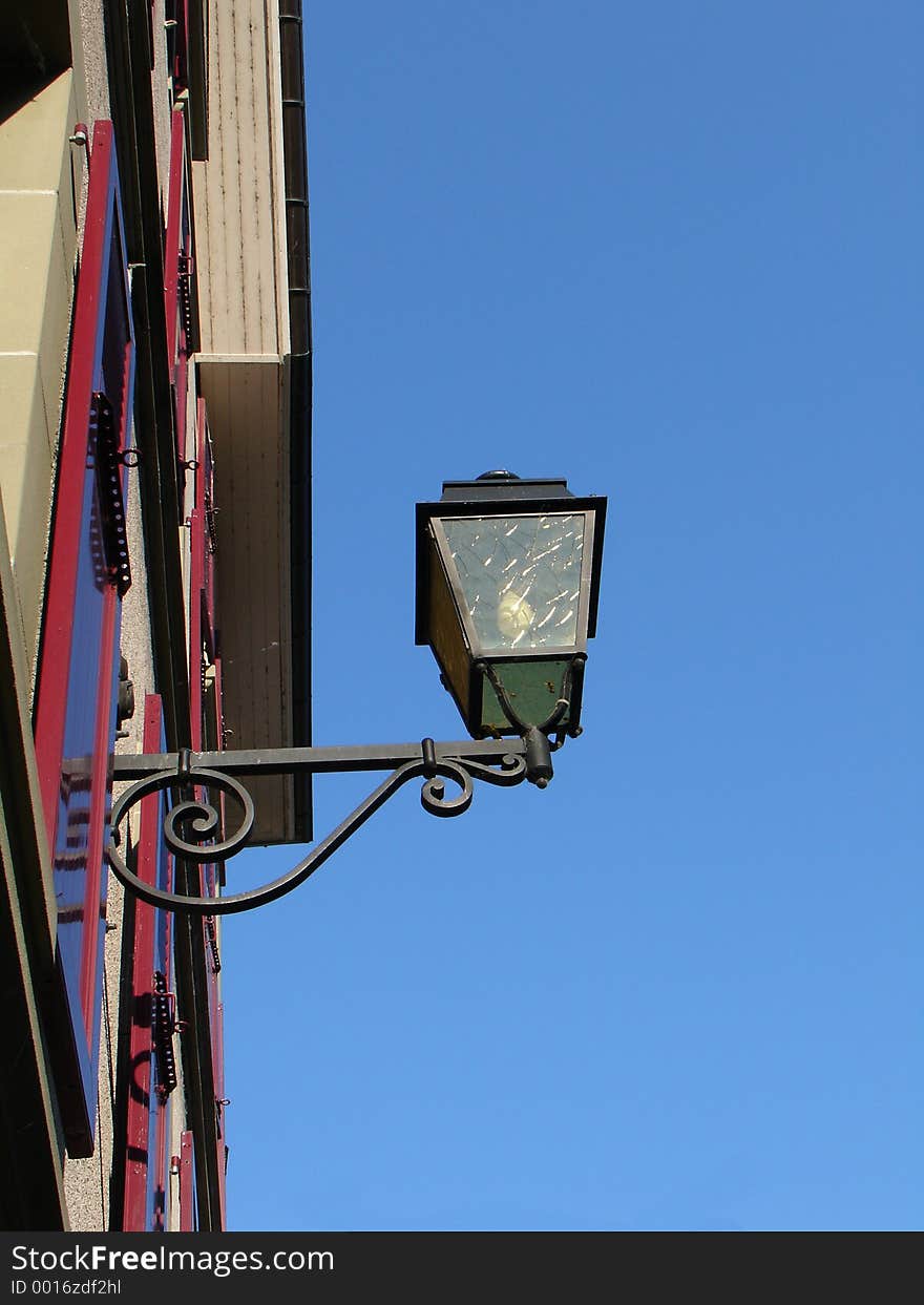 Street light mounted on a house wall on blue sky background. Street light mounted on a house wall on blue sky background