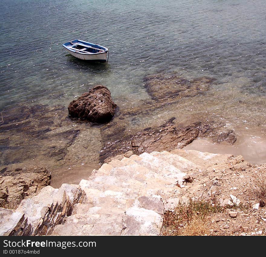 Stone tile steps leading to the shore with an old row boat in the greek islands